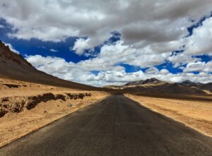 Travel forward concept background - road on plains in Himalayas with mountains and dramatic clouds. Manali-Leh road, Ladakh, Jammu and Kashmir, India