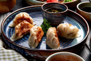 side view of traditional asian dumplings with meat and vegetables served with soy sauce on a plate on rustic background